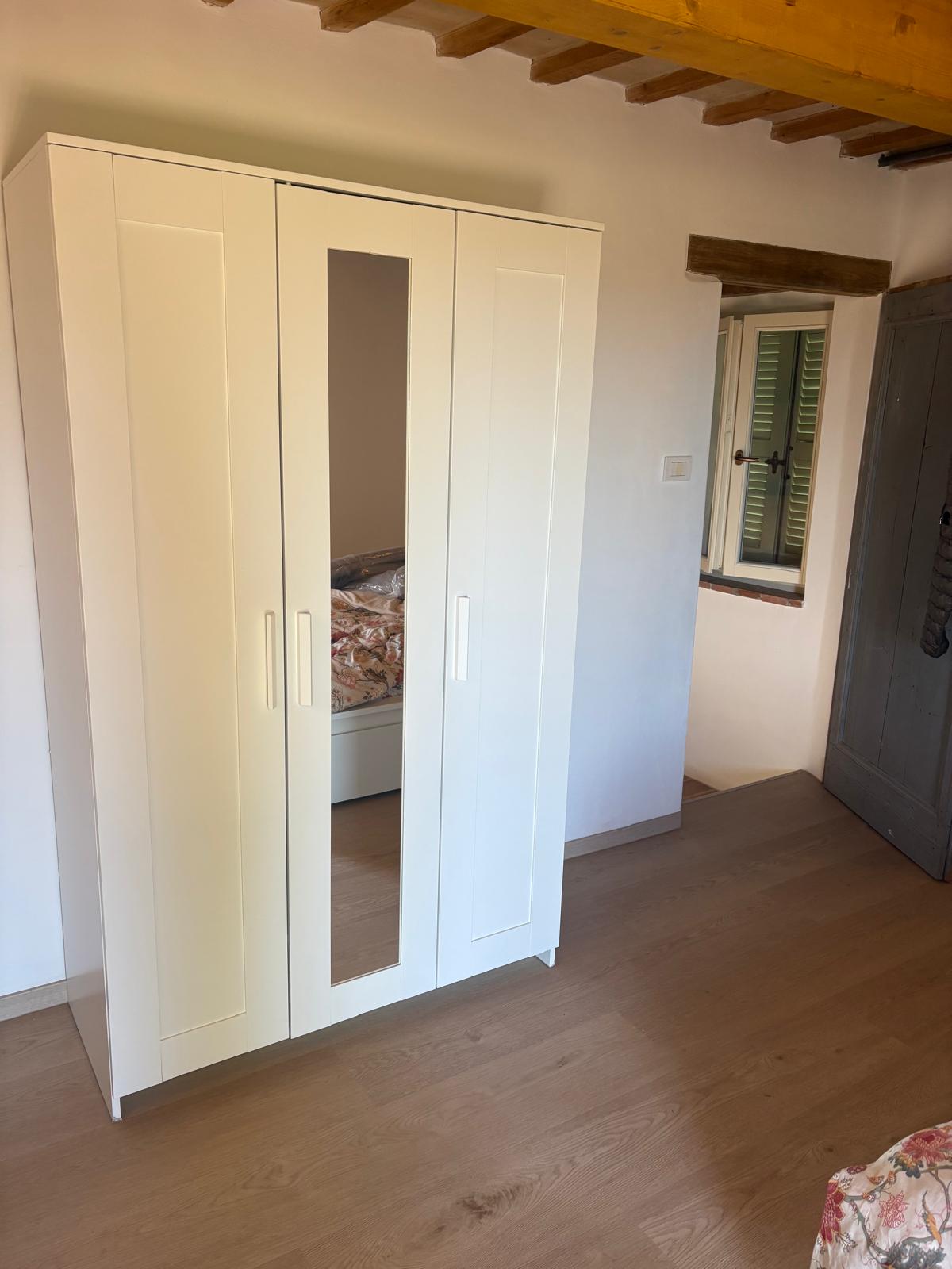 A bedroom with a beamed ceiling and a shuttered window